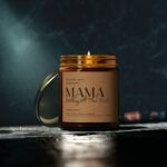 Amber glass jar holding lavender soy candle. Words on front MAMA-Holding All Their Firsts