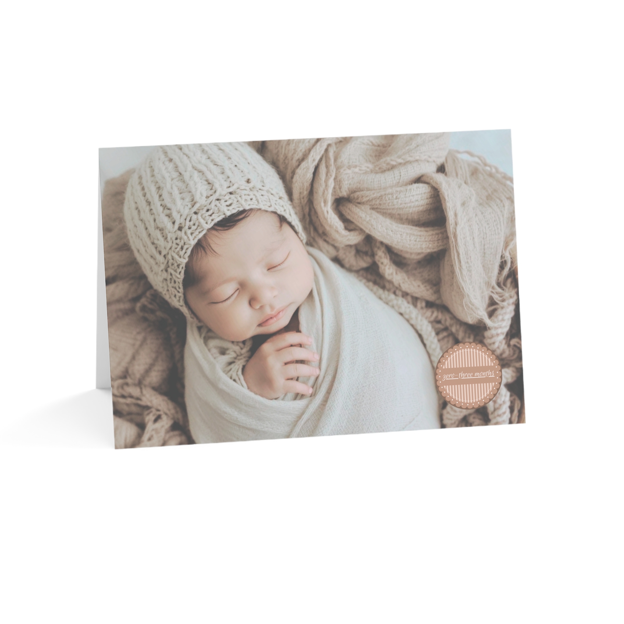Picture of Caucasian Baby Card 0-3 Months with baby wearing a knit hat on a beige blanket with the words zero-three months in a medallion on the front of the card.