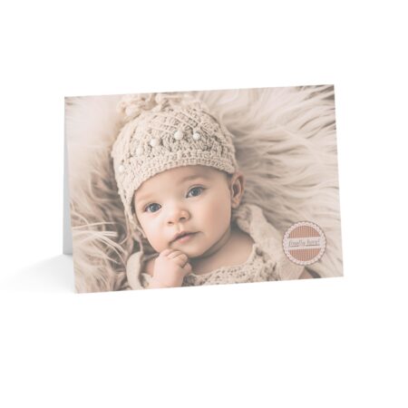 Finally Here card with Caucasian appearing baby wearing a knit hat on a beige blanket with the words Finally Here in a medallion on the front of the card.